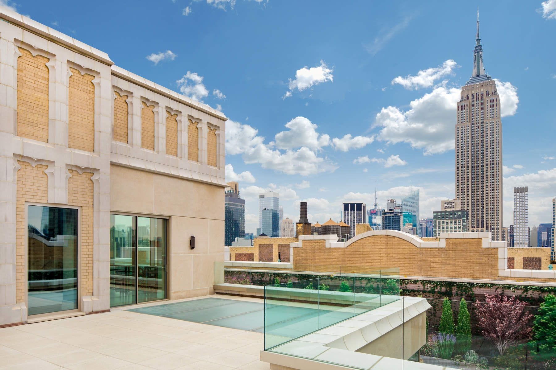 Rooftop patio with glass railing and city skyline view, prominent tall building in background under a cloudy blue sky.