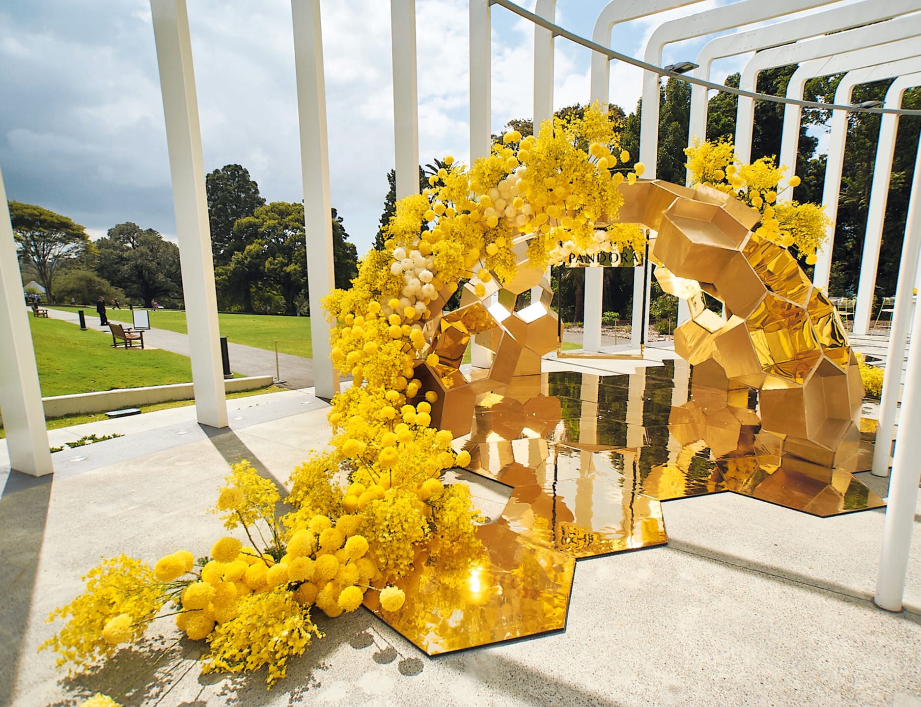 Golden floral arch decorated with yellow flowers and geometric shapes in an outdoor park setting under a clear sky.