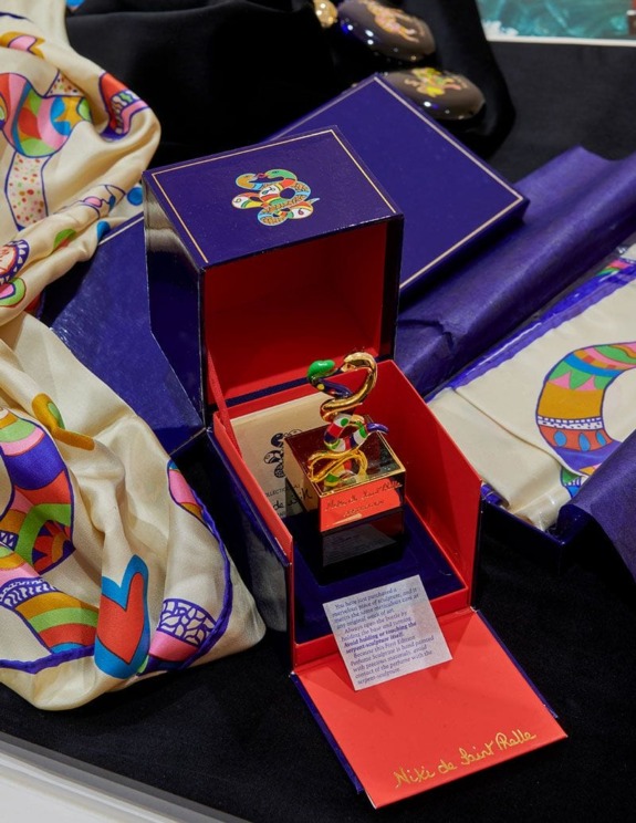 Colorful perfume bottle in an open box with vibrant scarves and decorative packaging displayed on a dark surface.