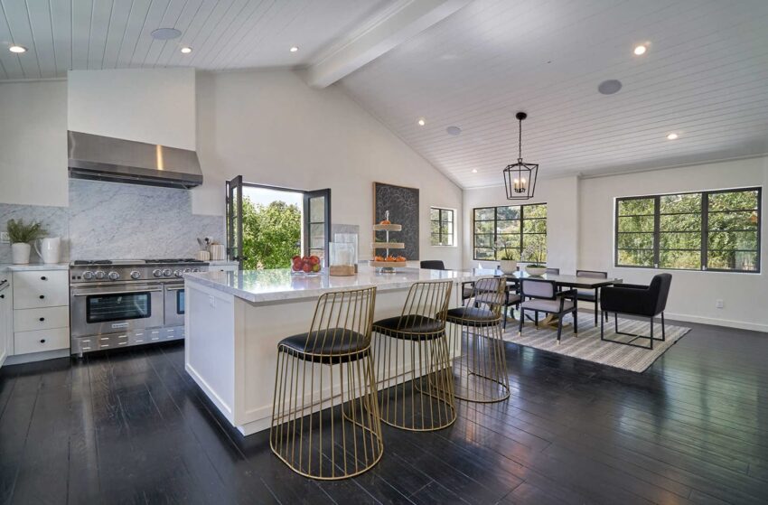 Modern open kitchen and dining area with large windows, marble countertop, bar stools, hardwood floors, and high ceilings.