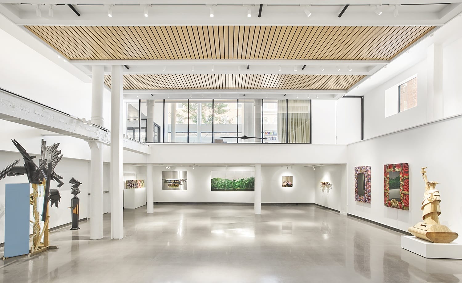 Modern art gallery interior with sculptures and paintings displayed on white walls under natural light.