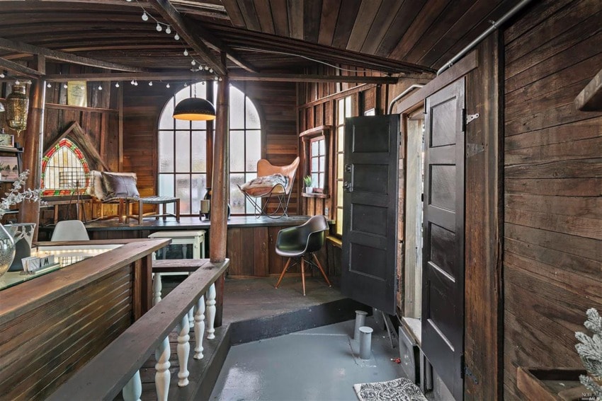 Rustic wooden loft with arched windows, dark furniture, and stained glass accents, creating a cozy, eclectic ambiance.