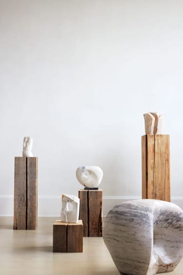 Marble sculptures displayed on wooden pedestals in a minimalist gallery setting.
