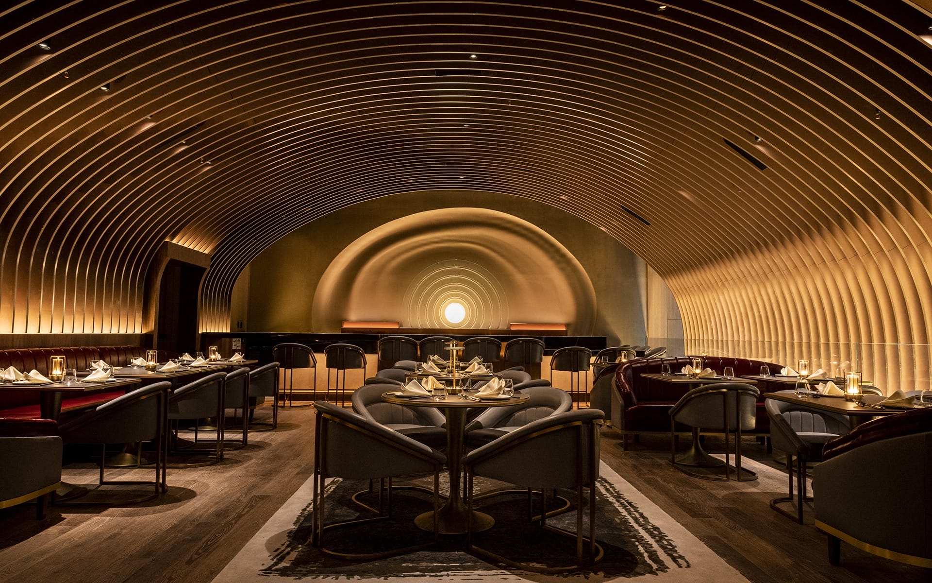 Elegant restaurant interior with arched ceiling, soft lighting, round tables, and velvet chairs set for dining.