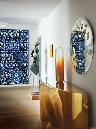 Contemporary hallway with artistic decor, including a sleek gold console, abstract sculpture, and a large oval mirror on the wall.