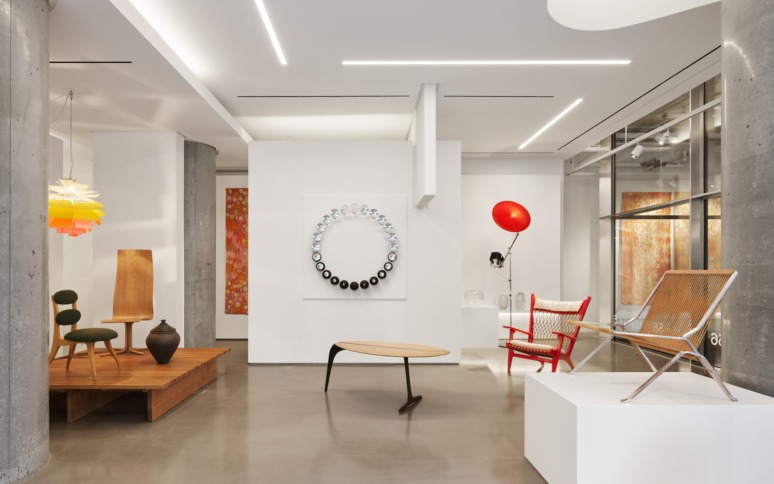 Modern gallery interior with contemporary furniture, colorful lamps, abstract art, and sleek concrete columns.