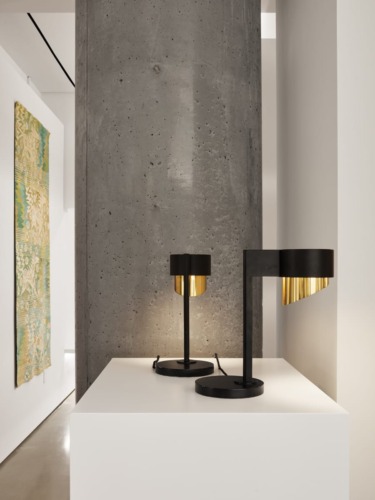 Modern black and gold table lamps on a white stand beside a large concrete column in a contemporary interior setting.