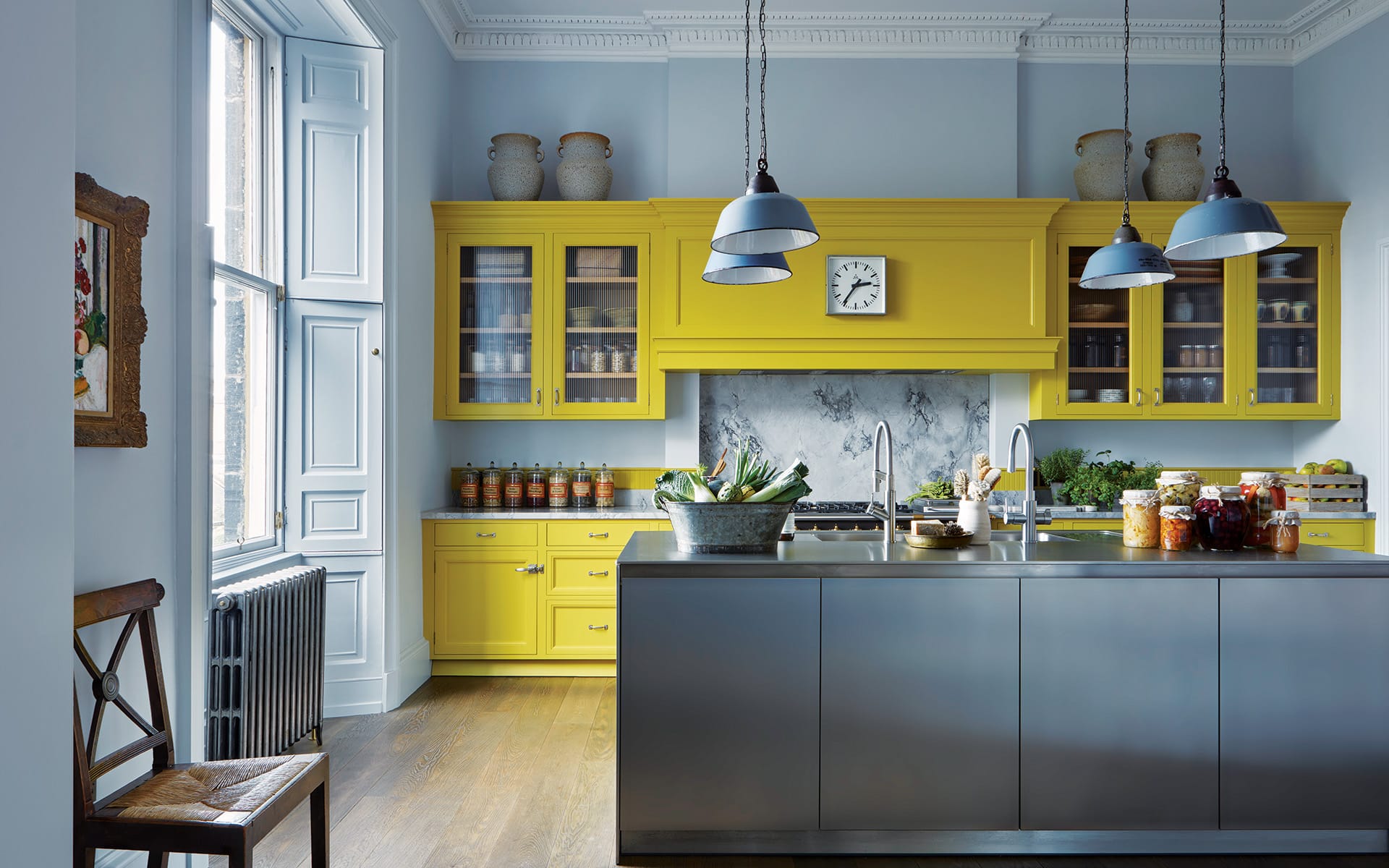 Modern kitchen with vibrant yellow cabinets, marble backsplash, gray island, pendant lights, and large windows.