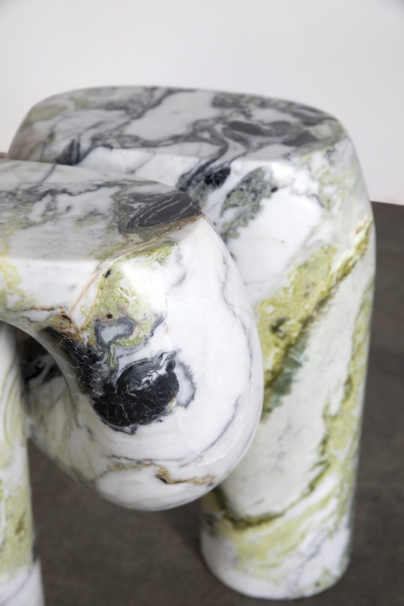 Close-up of a sculptural marble chair with green, white, and black swirling patterns on a gray background.