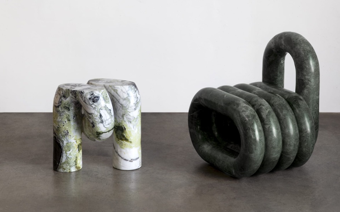 Two abstract marble sculptures on a gray floor, one in green and white, the other in dark green, with a minimalist background.