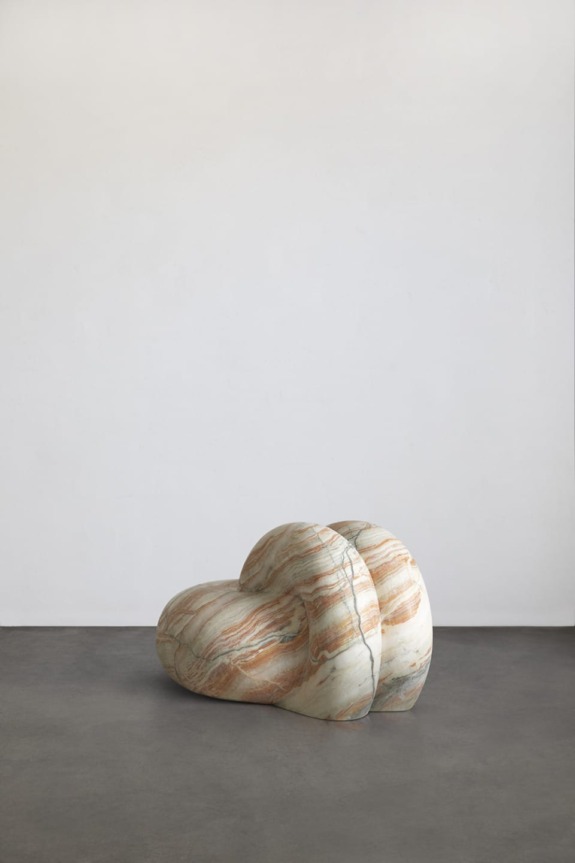 Marble sculpture resembling a cloud with a smooth texture, placed on a gray floor against a plain white wall.