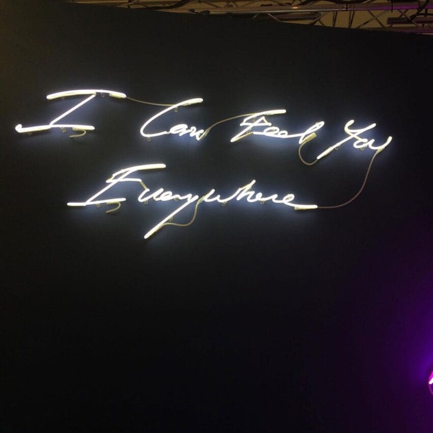 Neon sign with cursive text saying "I Can Feel You Everywhere" against a dark background.