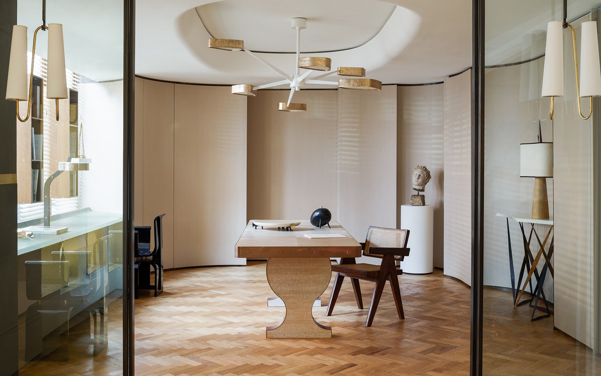 Modern office interior with wooden desk, chair, parquet floor, abstract light fixtures, and decorative art pieces.
