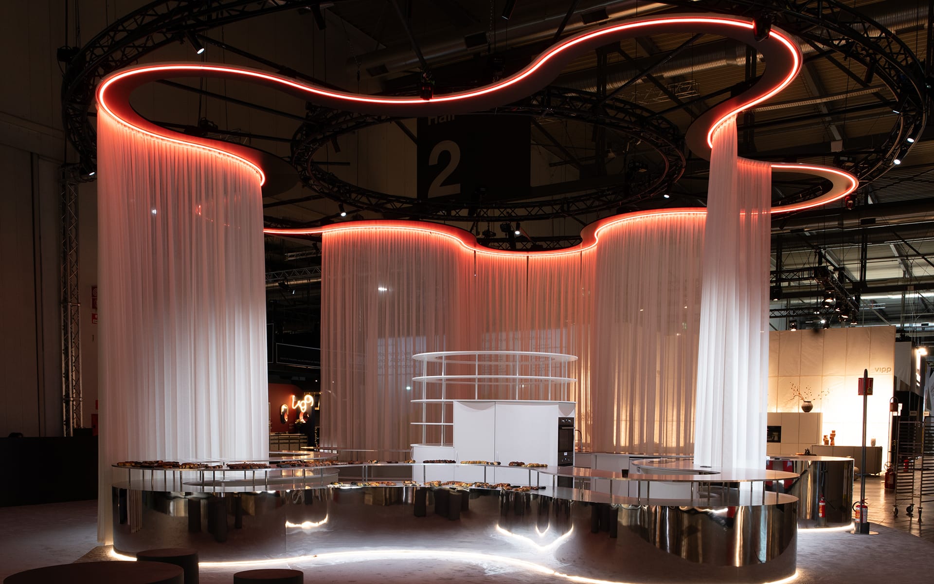 Modern exhibition booth with flowing white fabric partitions and glowing red neon accents at a trade show.