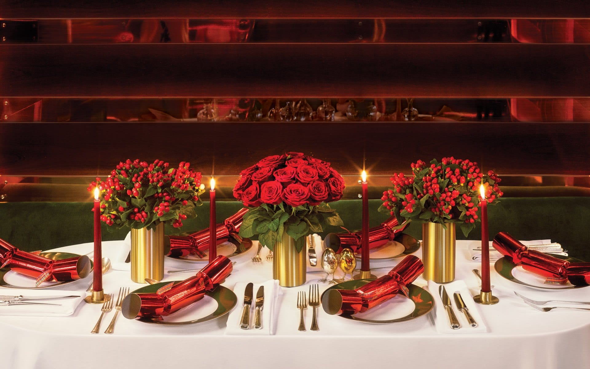 Elegant dining table set with red roses, candles, and gold accents for a festive or romantic celebration.