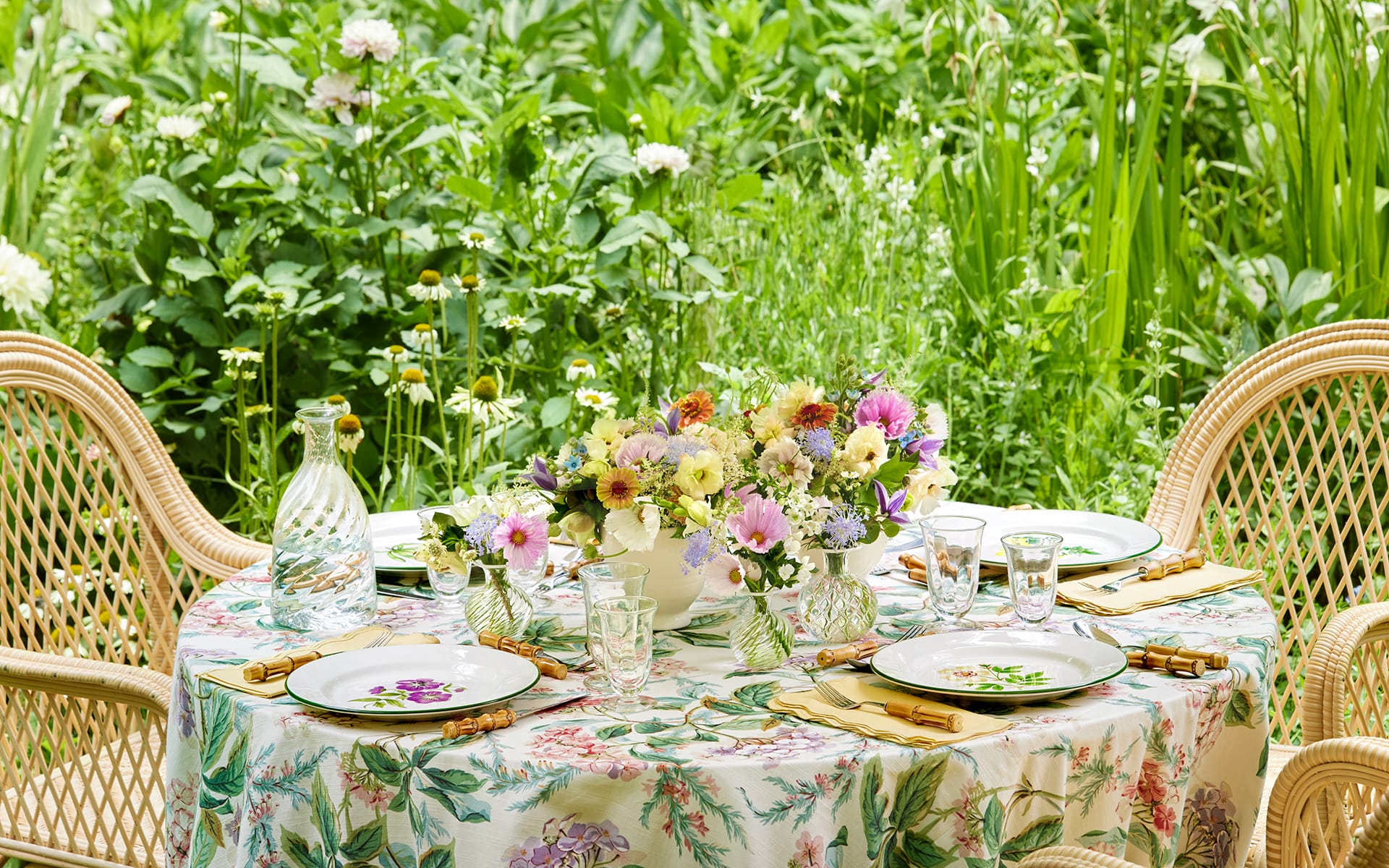 Zinnia, tweedia, cupcake cosmos, astilbe, hellebores, clematis, and butterfly ranunculus flowers in a bouquet placed on a flowered tablecloth, Italian hand-painted Florentina plates, and embroidered Fiore napkins from Aerin Lauder’s namesake lifestyle brand Aerin.