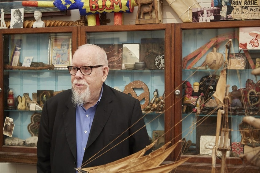 A person with glasses standing in front of display cabinets filled with various artifacts and memorabilia.