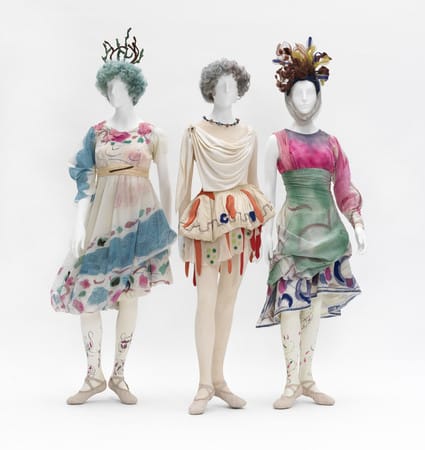Three mannequins wearing colorful, artistic costumes with unique headpieces against a plain background.