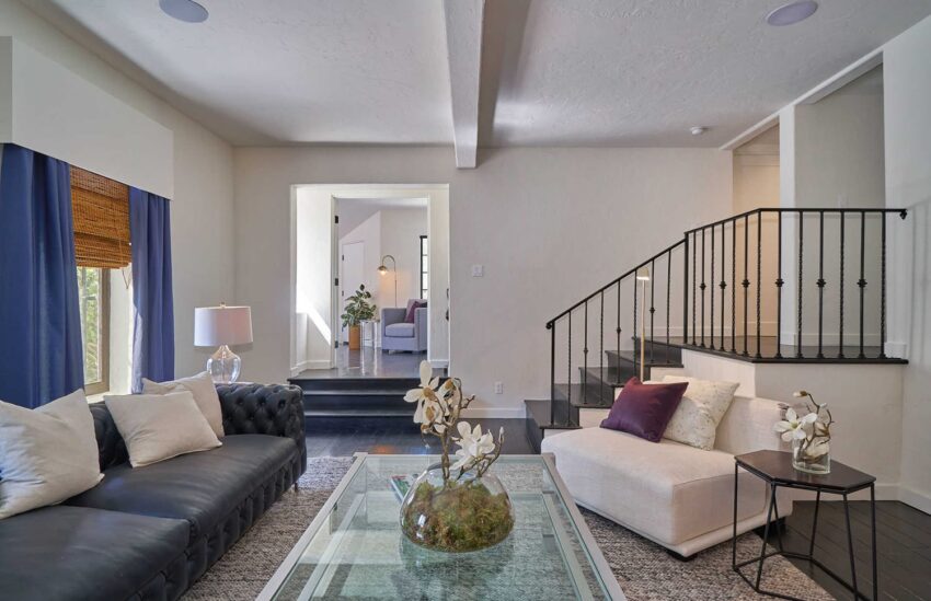 Modern living room with black sofa, white armchair, glass coffee table, and staircase leading to another room.