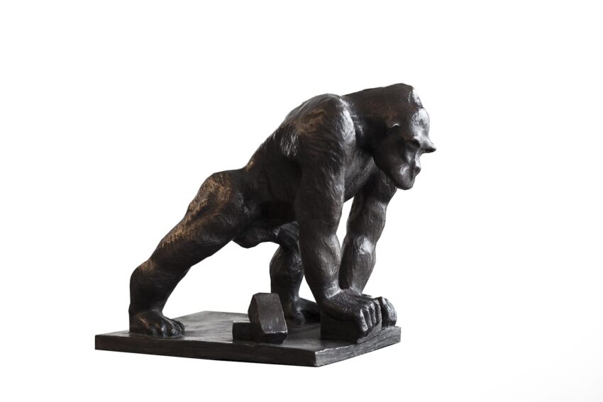 Bronze gorilla sculpture in a dynamic pose, leaning forward with one fist on the ground, displayed on a rectangular base.