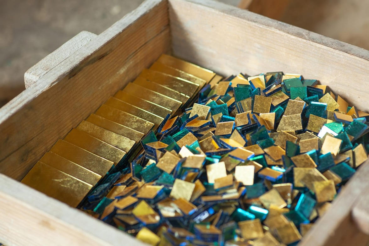 Wooden box filled with assorted gold and teal glass mosaic tiles ready for crafting or decoration projects.