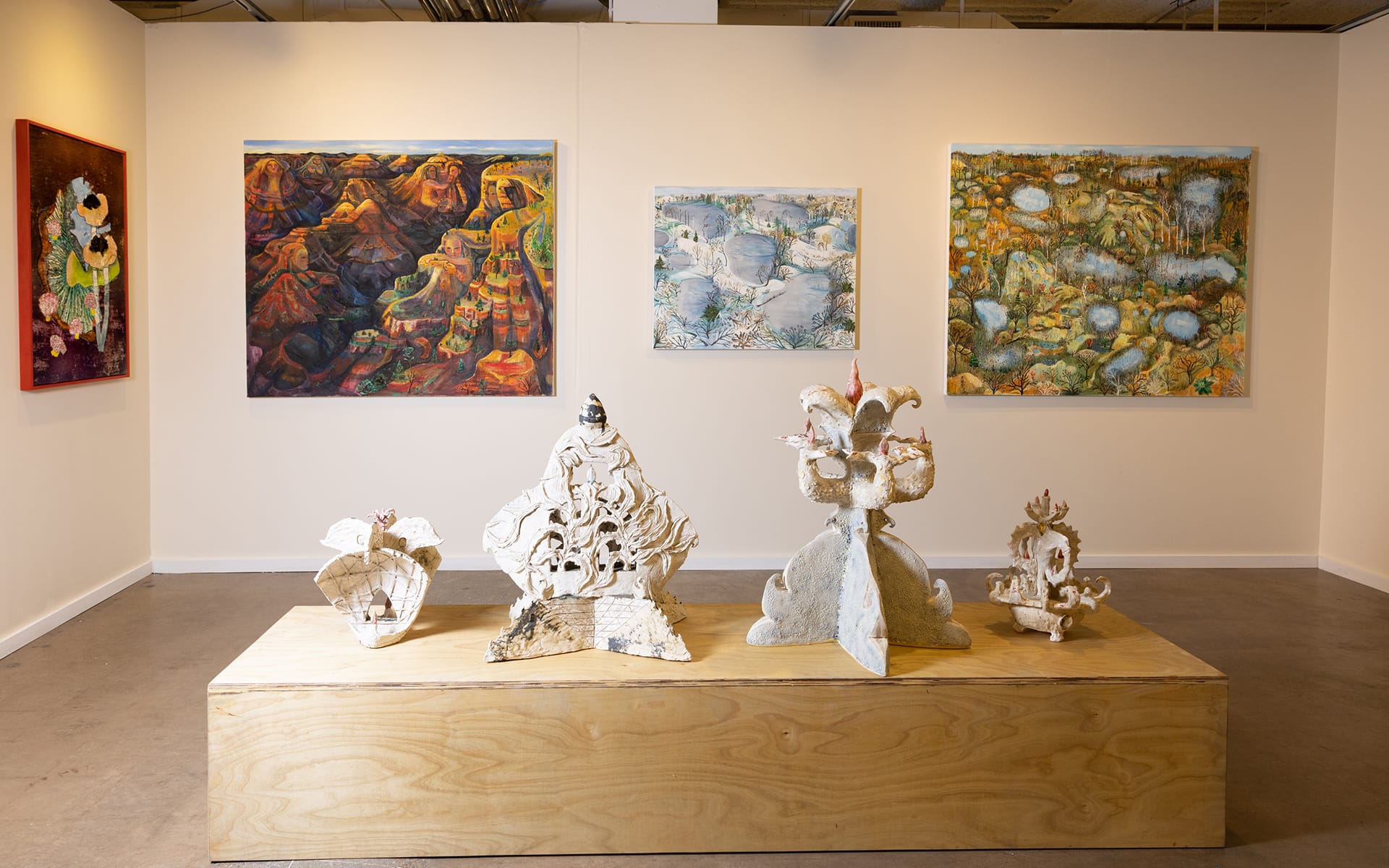 Art gallery display with colorful abstract paintings on the wall and unique sculptural pieces on a wooden platform in the foreground.