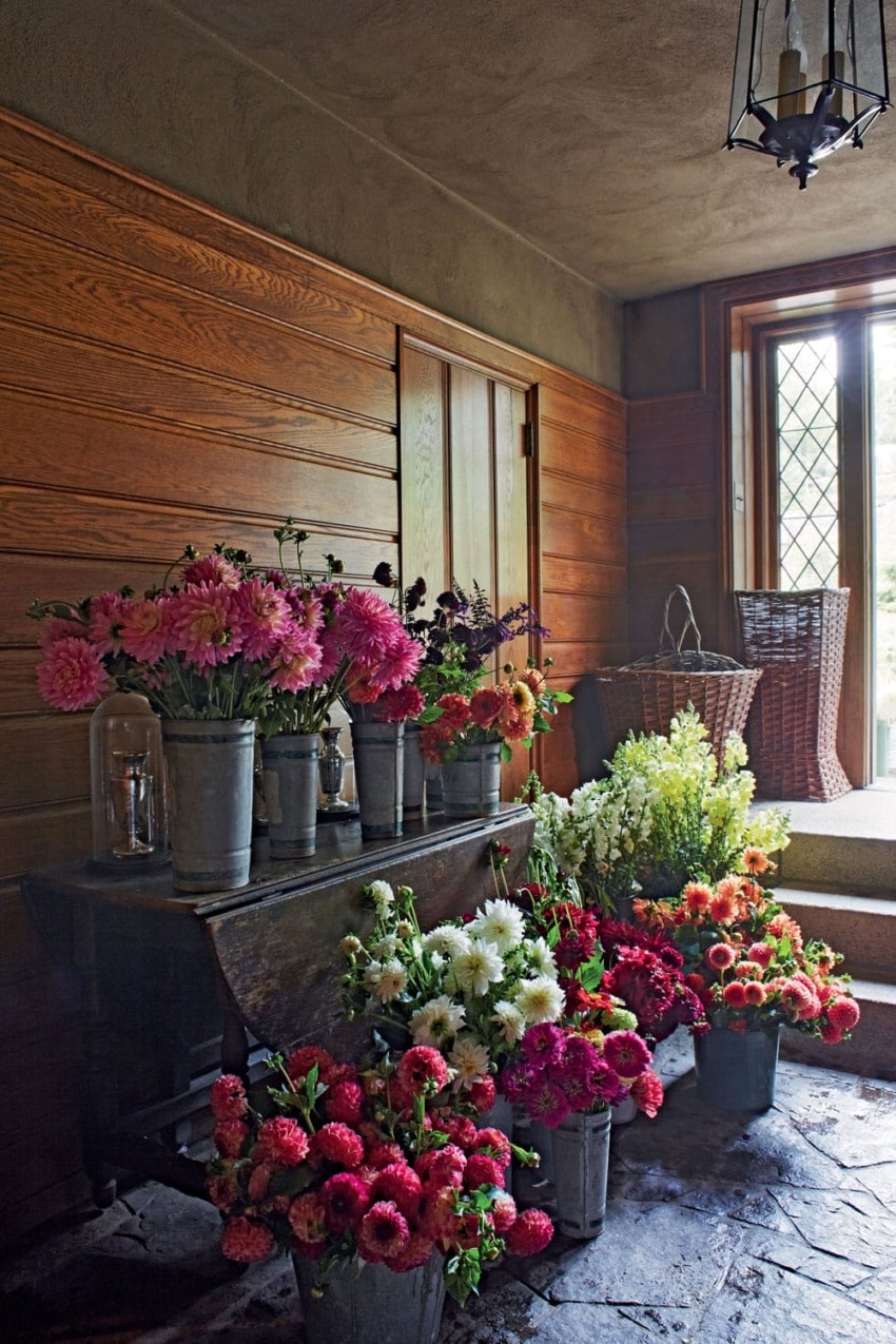 Room with wooden walls, large window, and colorful flowers in metal buckets on a stone floor.