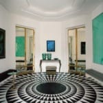 Art deco room with geometric patterned floor, green artwork, mirrored doors, and ornate console table with vases.