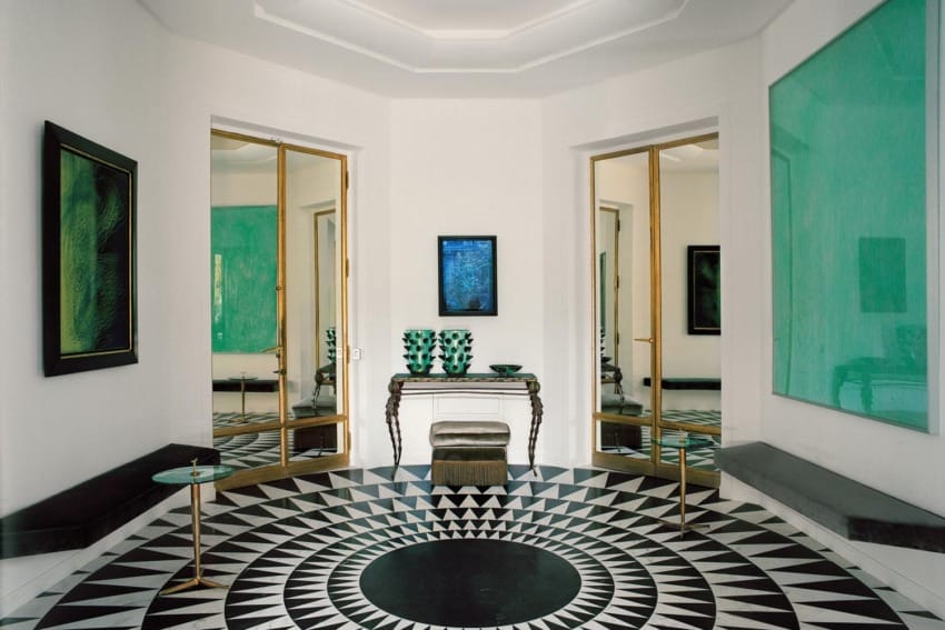 Art deco room with geometric patterned floor, green artwork, mirrored doors, and ornate console table with vases.