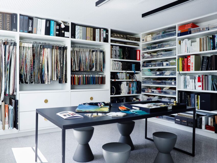 Interior design studio with a large table, fabric samples, and organized shelves filled with books and materials.