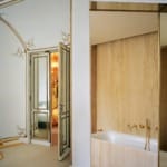 Elegant bathroom with gold fixtures, marble walls, and a door leading to a room with ornate decor and large mirror.