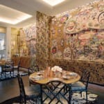 Colorful dining room with abstract mural, black chairs, round table set with flowers, and intricate wall designs.