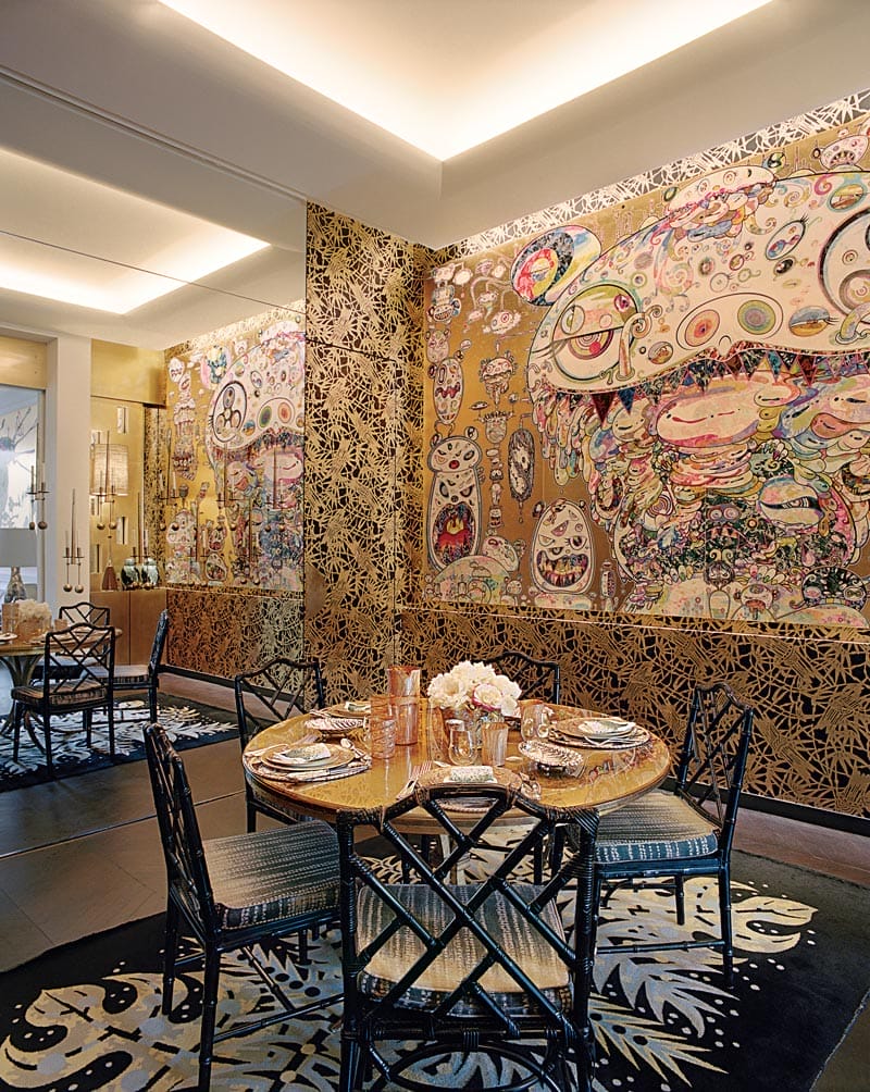 Colorful dining room with abstract mural, black chairs, round table set with flowers, and intricate wall designs.