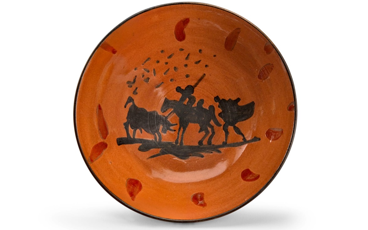 Orange ceramic plate featuring black silhouettes of a donkey, a man, and birds in the center, with decorative patterns.