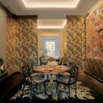 Dining room with patterned wallpaper, an art piece, round table, and chairs on a decorative rug