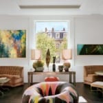 Elegant living room with large abstract chair, vibrant paintings, and a view of a city street through a large window.