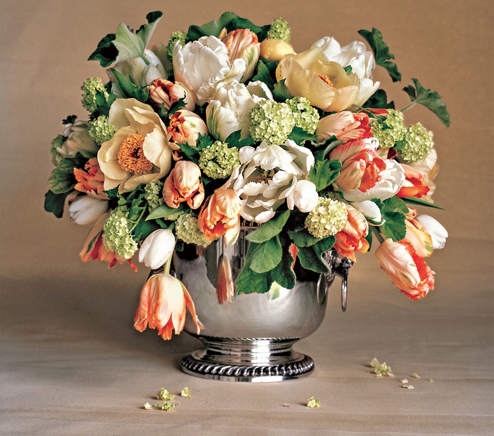 A colorful bouquet of tulips and peonies in a silver vase on a neutral background.
