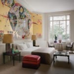 Modern bedroom with large abstract wall art, double bed, side tables with lamps, large window, chairs, and a small table.