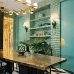 Dining room with teal geometric wall pattern, brass table, black chairs, and modern lighting fixture.