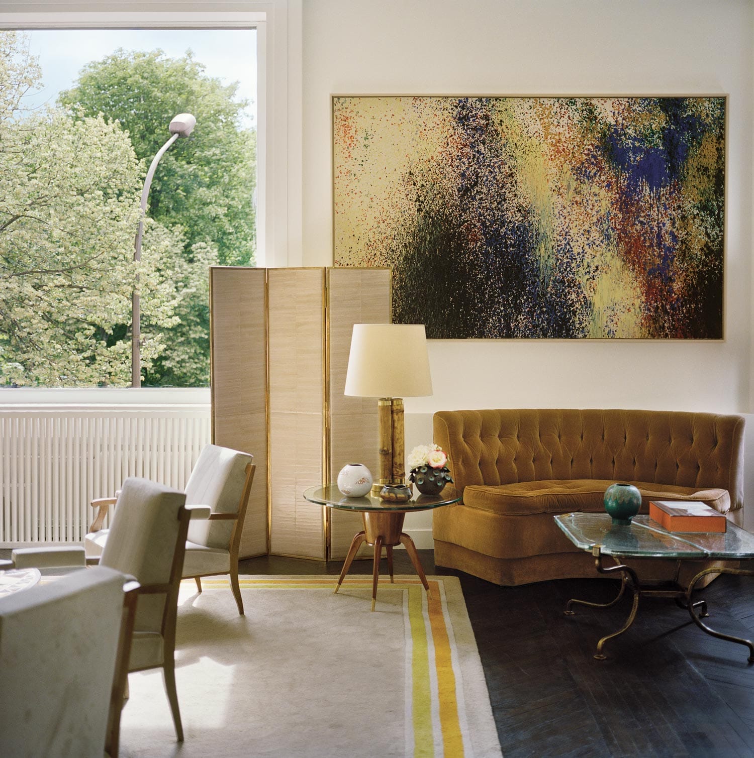 Modern living room with abstract painting, vintage furniture, floor lamp, large window, and garden view.