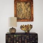 A textured table with a lamp, artistic vase, and framed abstract painting hanging on a white wall.