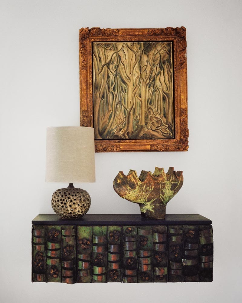 A textured table with a lamp, artistic vase, and framed abstract painting hanging on a white wall.