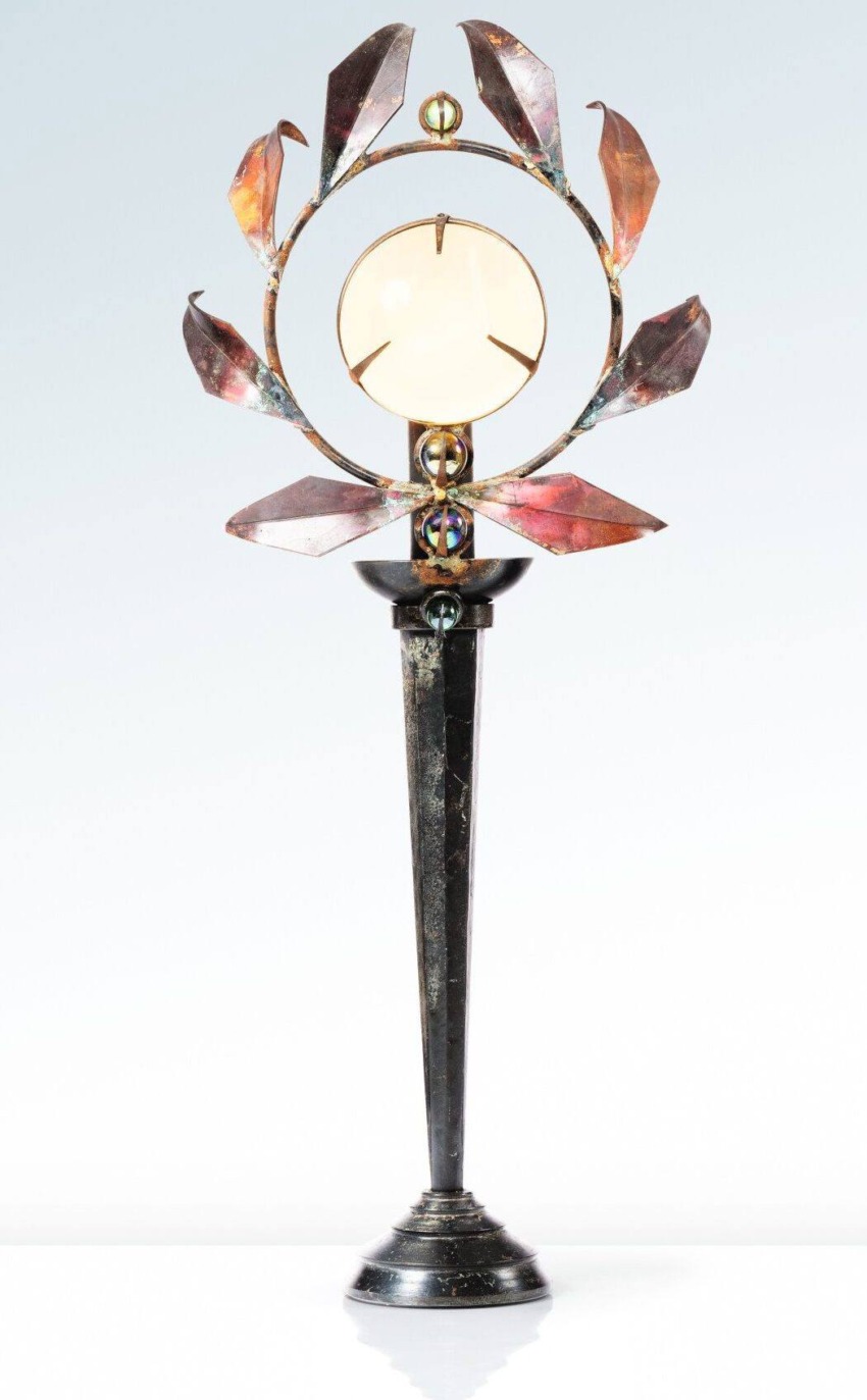 Decorative metal sculpture with leaf-like details on a tall stand, featuring a circular center piece against a light background