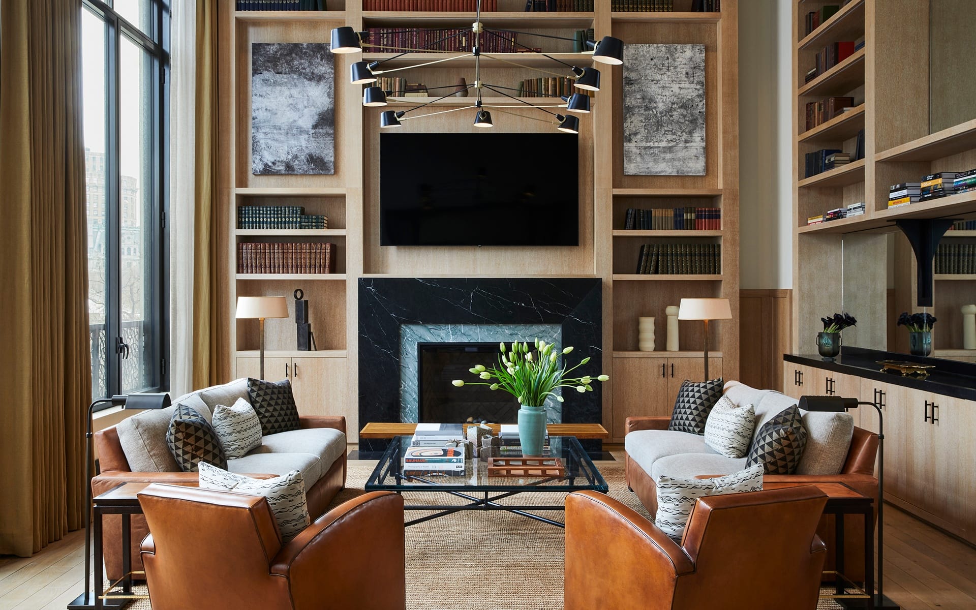 Modern living room with leather chairs, sofas, a fireplace, and a large bookshelf.