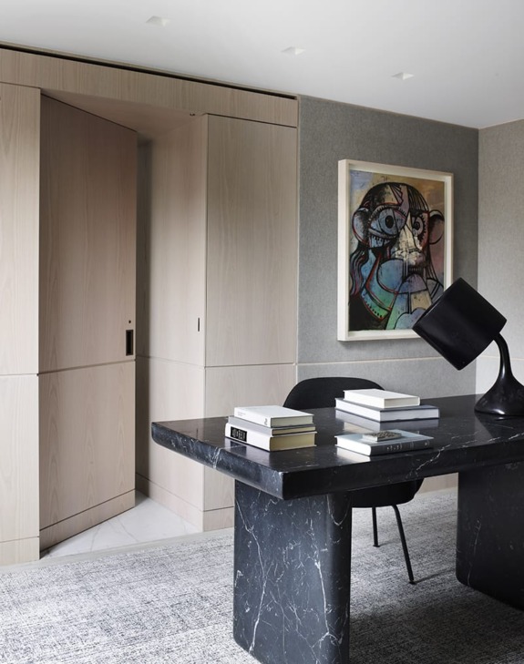 Modern office with black marble desk, angled lamp, books, gray walls, and abstract artwork on the wall.