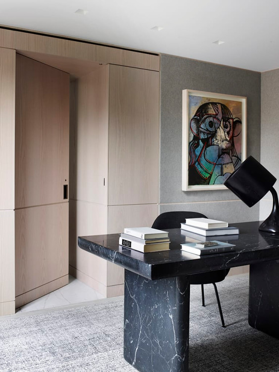 Modern office with black marble desk, angled lamp, books, gray walls, and abstract artwork on the wall.