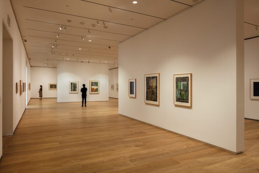 People viewing paintings in a modern art gallery with white walls and wooden floors.