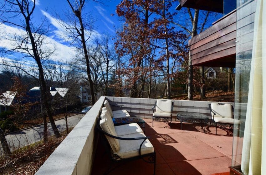 Spacious outdoor balcony with seating and a view of trees and houses on a clear sunny day.