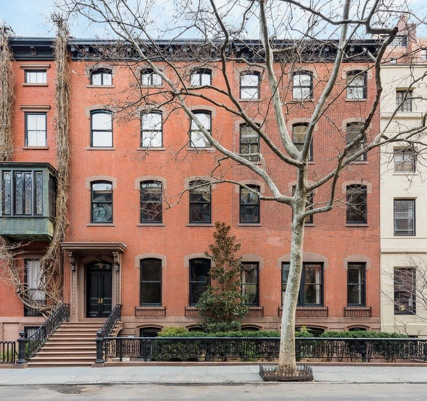 Historic red brick townhouse with black detailing, large bay windows, and a bare tree in front on a quiet city street.