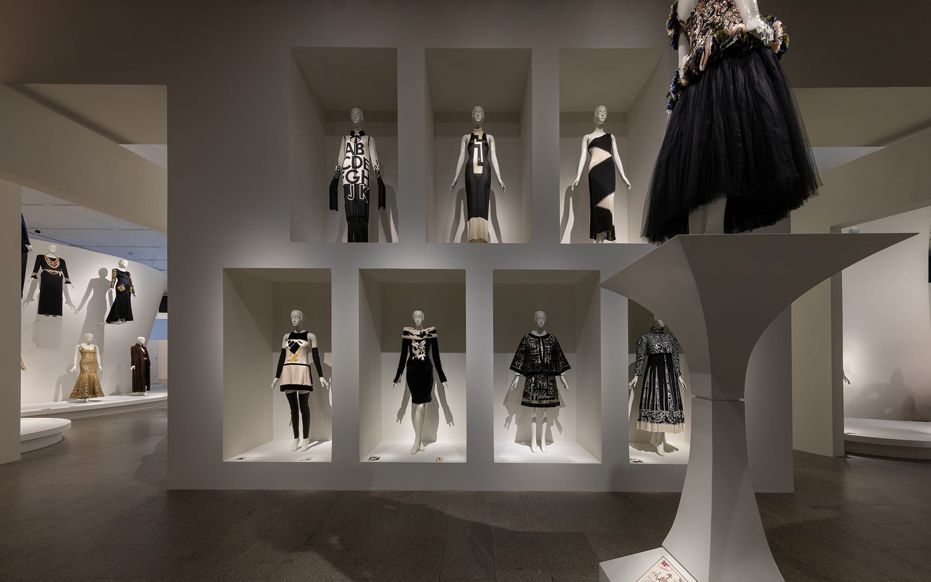Fashion exhibition showcasing avant-garde black and white dresses on mannequins in a modern gallery setting.